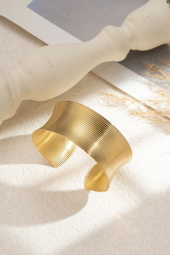 Detalle de líneas grabadas en brazalete ancho estriado en acero dorado