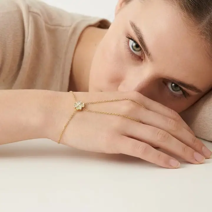 Pulsera de mano con trébol brillante en acero dorado.