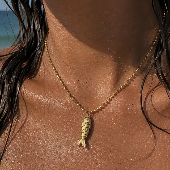 Detalle de colgante de pez con circonita en collar de acero bañado en oro de 18k